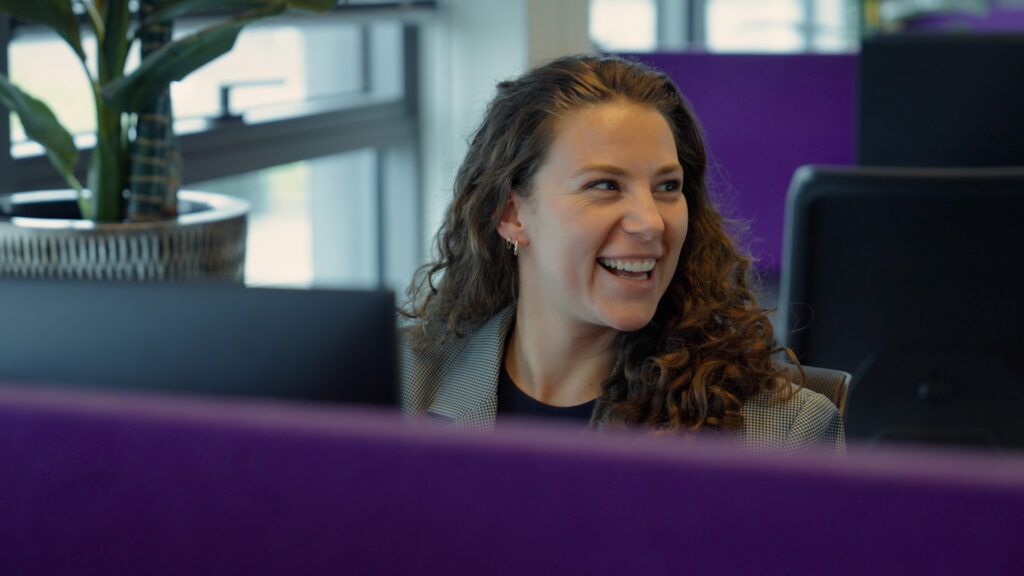 Een lachende vrouwelijke medewerker van Vonders met krullend haar achter haar bureau op het kantoor voor arbeidsbemiddeling in de infra.